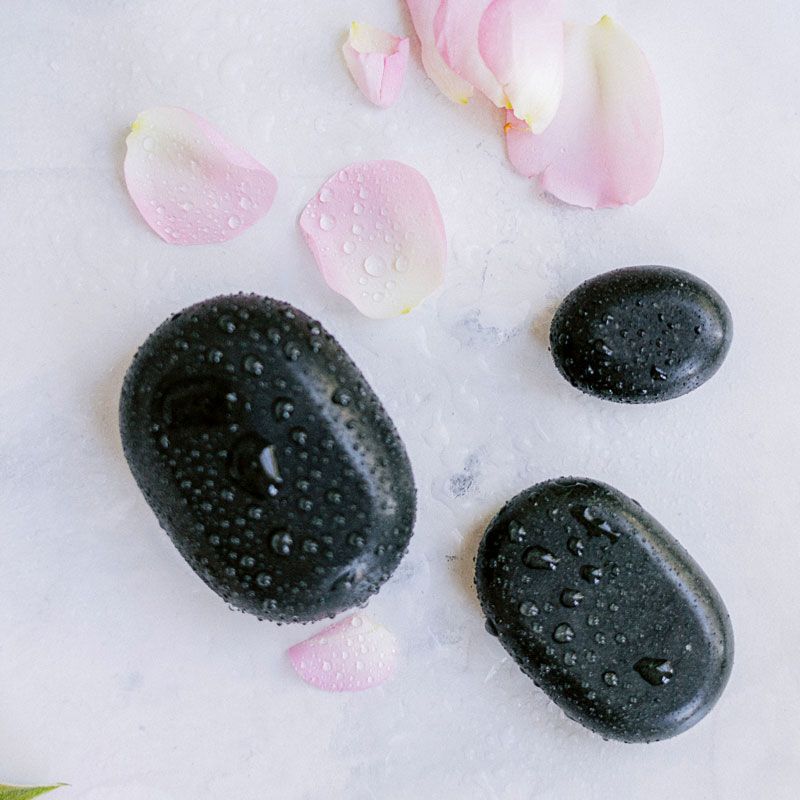 3 piedras lisas negras junto a 3 petalos de flor